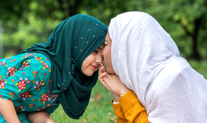 Wall Mural - Portrait of happy religious enjoy happy love asian islam family muslim mother and little muslim girls child with hijab dress smiling and having fun moments good time, islam, ramadan in summer park