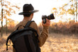 Arabic young photographer holding professional camera on the forest or park, back view. Man exploring a forest capturing the beauty in a digital camera.
