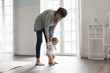 © fizkes - Cute toddler in bodysuit holding loving mothers hands and makes first steps in cozy bedroom, walk on warm floor with underfloor heating system. Adoption, care, happy motherhood, growth and development