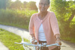 © Nicola Katie/peopleimages.com - Portrait, smile and elderly woman on bike outdoor, exercise and fitness in summer. Happy, senior person on bicycle in nature or garden for cycling in countryside for body health, travel and glasses