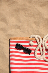 Wall Mural - Striped beach bag and sunglasses on sand, top view. Space for text