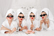 © wedmoments.stock - Young, beautiful women in bathrobes and glasses enjoying bachelorette party at spa or hotel and eating donuts, happy multiracial girlfriends celebrating bachelorette party