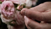 Man Hand Holding An Engagement Ring With His Fingers. Closeup. Man Makes A Marriage Proposal. Bouquet Of Pink Roses. Flowers And Jewelry For A Romantic Wedding Proposal.
