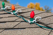 Hanging Christmas string lights on shingles of roof. Holiday decorating safety, lighting and accident prevention concept.