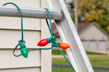 Christmas String Lights Hanging On Ladder Rung Outside Of House. Holiday Lighting Decorating, Ladder Safety And Accident Prevention Concept.