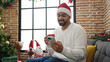 © Krakenimages.com - African american man using smartphone drinking coffee celebrating christmas at home