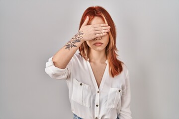 Sticker - Young caucasian woman standing over isolated background covering eyes with hand, looking serious and sad. sightless, hiding and rejection concept