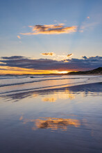 Cloud Formation And Sunset Reflected On A Wide Sandy Beach With Gentle Waves