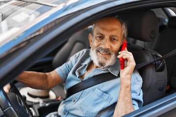 Wall Mural - senior grey-haired man talking on smartphone sitting on car at street