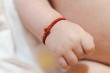 Closeup of a small hand of a newborn baby with a red bracelet encircling the wrist