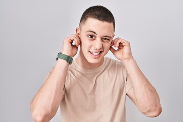 Canvas Print - Young man standing over isolated background covering ears with fingers with annoyed expression for the noise of loud music. deaf concept.