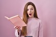 Young caucasian woman reading a book over pink background afraid and shocked with surprise and amazed expression, fear and excited face.