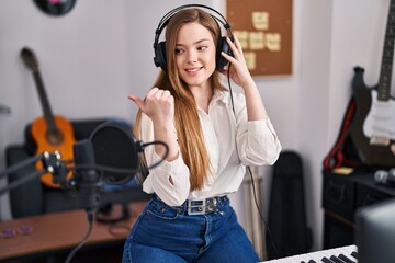 Poster - Young caucasian woman recording song at music studio pointing thumb up to the side smiling happy with open mouth