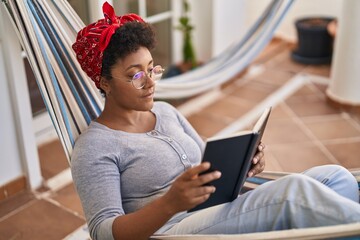 Poster - African american woman reading book lying on hammock at home terrace