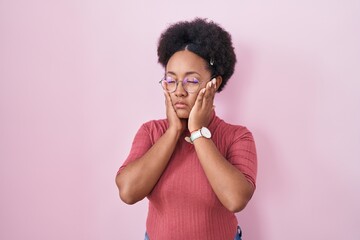 Wall Mural - Beautiful african woman with curly hair standing over pink background tired hands covering face, depression and sadness, upset and irritated for problem