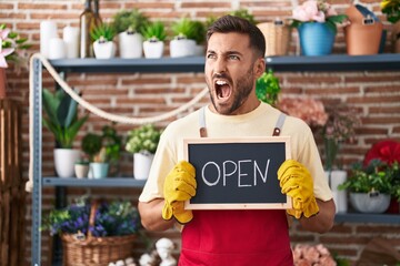 Wall Mural - Handsome hispanic man working at florist holding open sign angry and mad screaming frustrated and furious, shouting with anger. rage and aggressive concept.