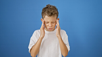 Poster - Adorable blond boy, alone and upset, standing against isolated blue background, suffering a stressful headache and the despair of a mental ache