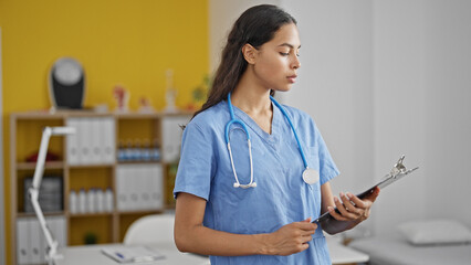 Canvas Print - African american woman doctor reading document on clipboard at clinic