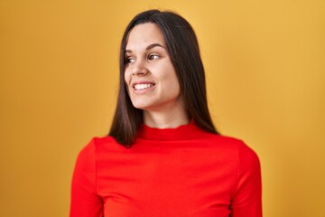 Canvas Print - Young hispanic woman standing over yellow background looking away to side with smile on face, natural expression. laughing confident.