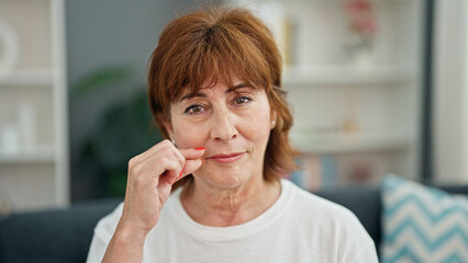 Poster - Middle age woman smiling confident sitting on sofa doing close mouth gesture home