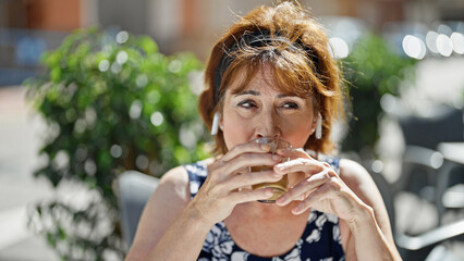 Wall Mural - Middle age woman listening to music drinking coffee at coffee shop terrace