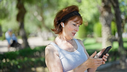 Canvas Print - Middle age woman using smartphone and earphones smiling at park