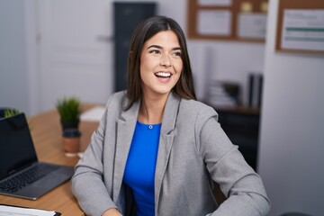 Young beautiful hispanic woman business worker smiling confident sitting on table at office