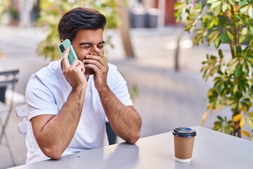 Poster - Young hispanic man talking on smartphone drinking coffee at coffee shop terrace