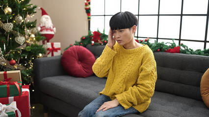 Wall Mural - Young chinese woman suffering for headache sitting by christmas tree at home