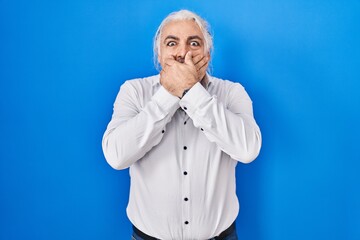 Wall Mural - Middle age man with grey hair standing over blue background shocked covering mouth with hands for mistake. secret concept.