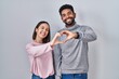 Young hispanic couple standing together smiling in love doing heart symbol shape with hands. romantic concept.