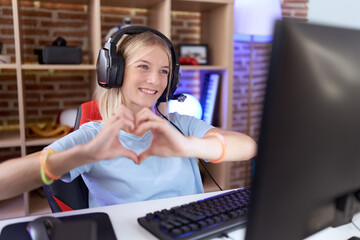 Wall Mural - Young caucasian woman playing video games wearing headphones smiling in love doing heart symbol shape with hands. romantic concept.