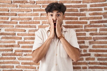 Poster - Arab man with beard standing over bricks wall background afraid and shocked, surprise and amazed expression with hands on face