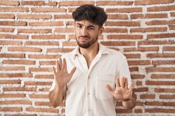 Wall Mural - Arab man with beard standing over bricks wall background moving away hands palms showing refusal and denial with afraid and disgusting expression. stop and forbidden.