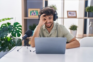 Wall Mural - Arab man with beard working at the radio smiling happy doing ok sign with hand on eye looking through fingers