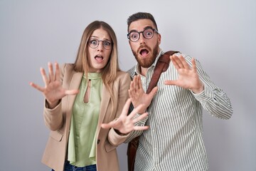 Wall Mural - Young couple standing over white background afraid and terrified with fear expression stop gesture with hands, shouting in shock. panic concept.