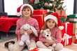 © Krakenimages.com - Brother and sister holding teddy bear sitting on floor by christmas tree at home