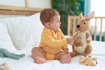 Sticker - Adorable toddler sitting on bed holding kangaroo doll at bedroom