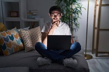 Sticker - Young hispanic man using laptop at home at night thinking worried about a question, concerned and nervous with hand on chin