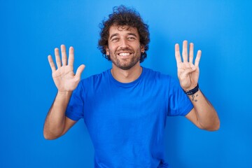 Poster - Hispanic young man standing over blue background showing and pointing up with fingers number nine while smiling confident and happy.