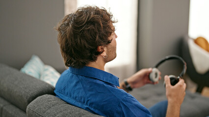 Poster - Young hispanic man sitting on sofa holding headphones at home