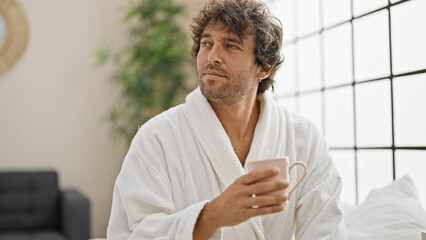 Canvas Print - Young hispanic man wearing bathrobe drinking coffee at bedroom