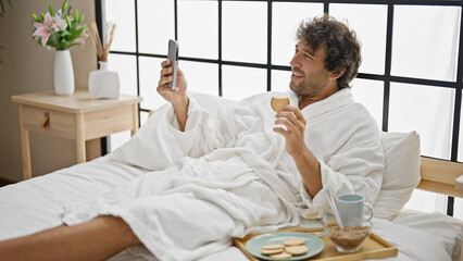 Wall Mural - Young hispanic man having breakfast doing video call at bedroom