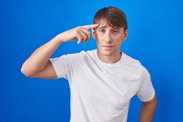 Sticker - Caucasian blond man standing over blue background pointing unhappy to pimple on forehead, ugly infection of blackhead. acne and skin problem