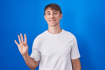 Sticker - Caucasian blond man standing over blue background showing and pointing up with fingers number four while smiling confident and happy.