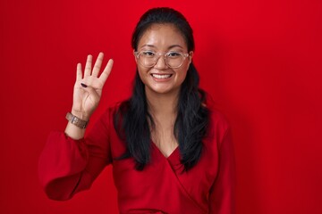 Canvas Print - Asian young woman standing over red background showing and pointing up with fingers number four while smiling confident and happy.