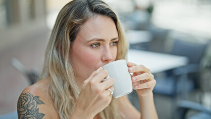 Wall Mural - Young blonde woman drinking coffee sitting on table at coffee shop terrace