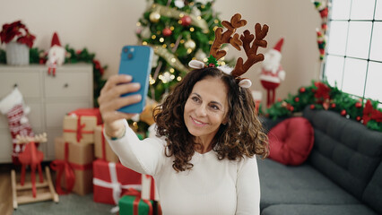 Canvas Print - Middle age hispanic woman make selfie by smartphone sitting on floor by christmas tree at home