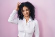 Hispanic woman with curly hair standing over pink background worried and stressed about a problem with hand on forehead, nervous and anxious for crisis