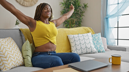 Canvas Print - African american woman sitting on sofa stretching arms tired at home